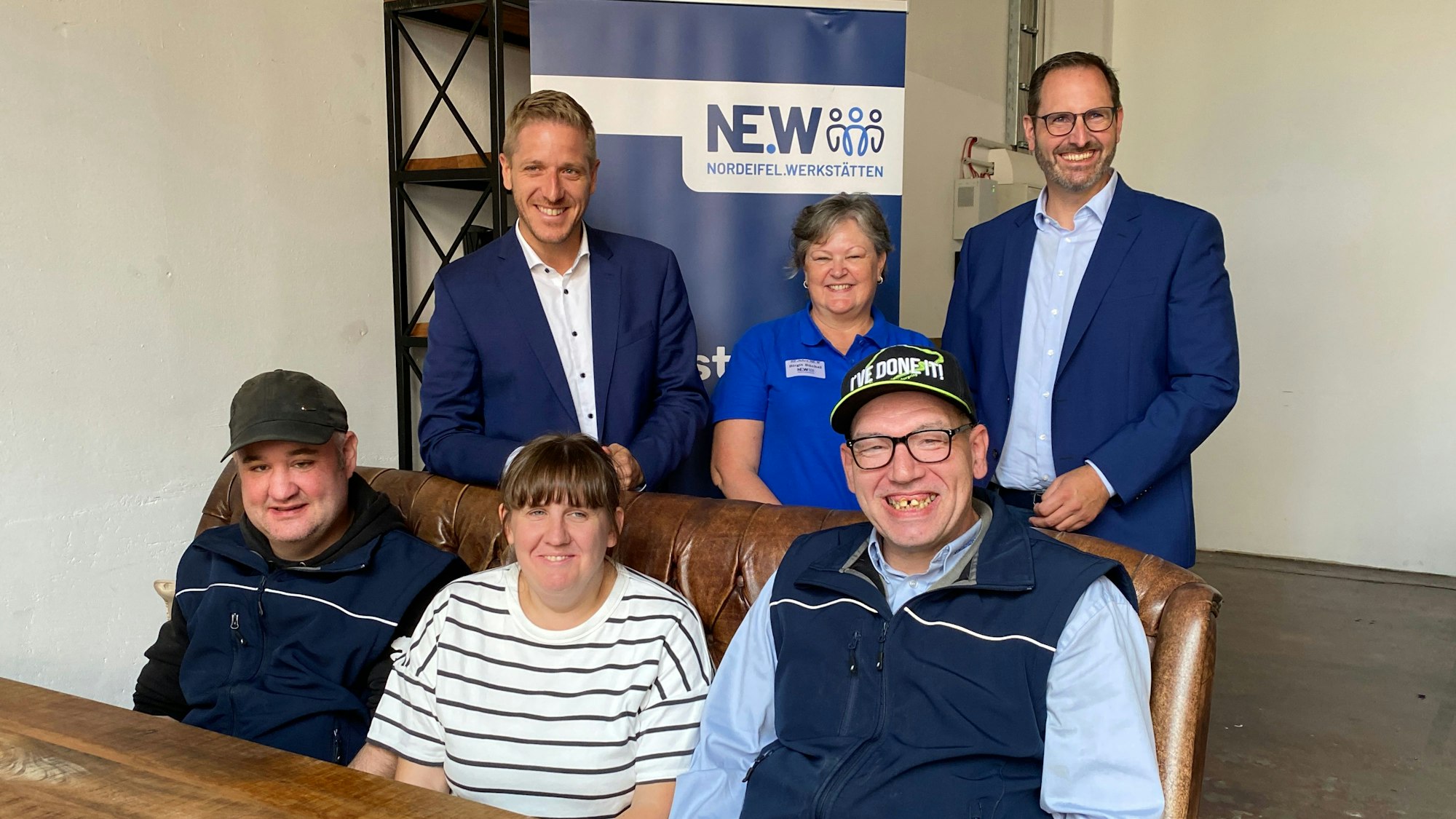 Zwei Frauen und vier Männer sitzen und stehen in zwei Reihen nebeneinander.