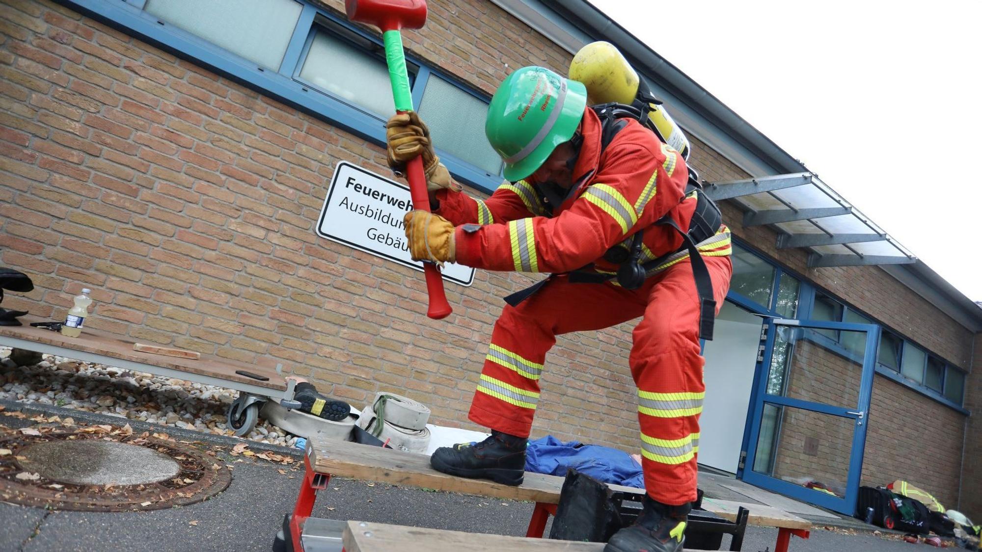 Ein Mann in roter Feuerwehrkleidung schlägt mit einem Vorschlaghammer auf ein schwarzen Stahlblock.