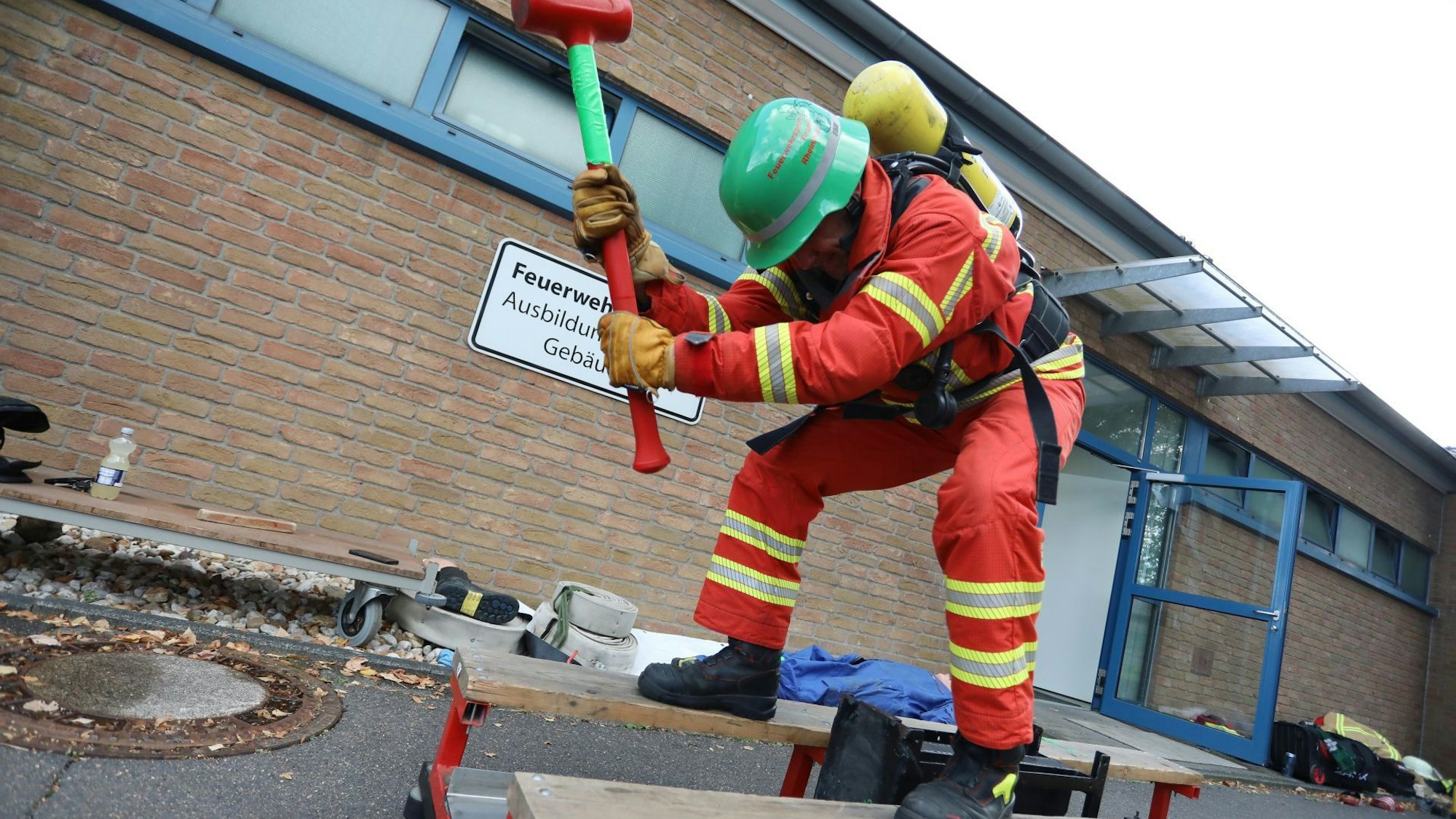 Ein Mann in roter Feuerwehrkleidung schlägt mit einem Vorschlaghammer auf ein schwarzen Stahlblock.