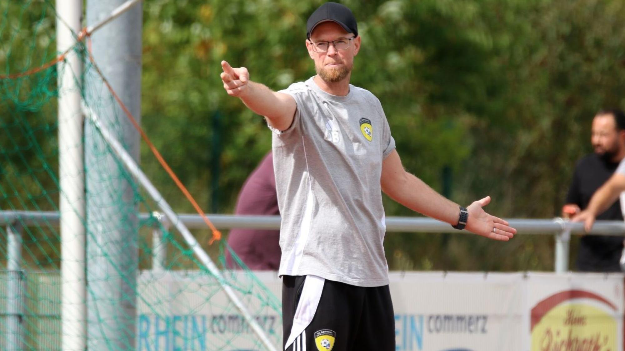 Daniel Bartsch trägt eine schwarze Kappe und hat die Arme ausgebreitet. Mit dem rechten Zeige- und Mittelfinger deutet er in einer Richtung.