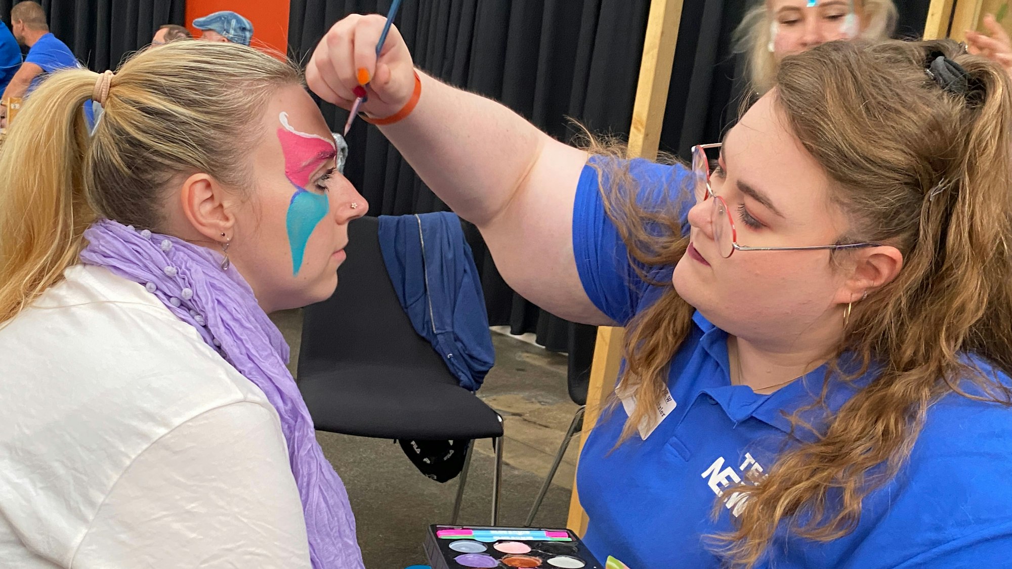 Eine Frau lässt sich von einer anderen bunt schminken.