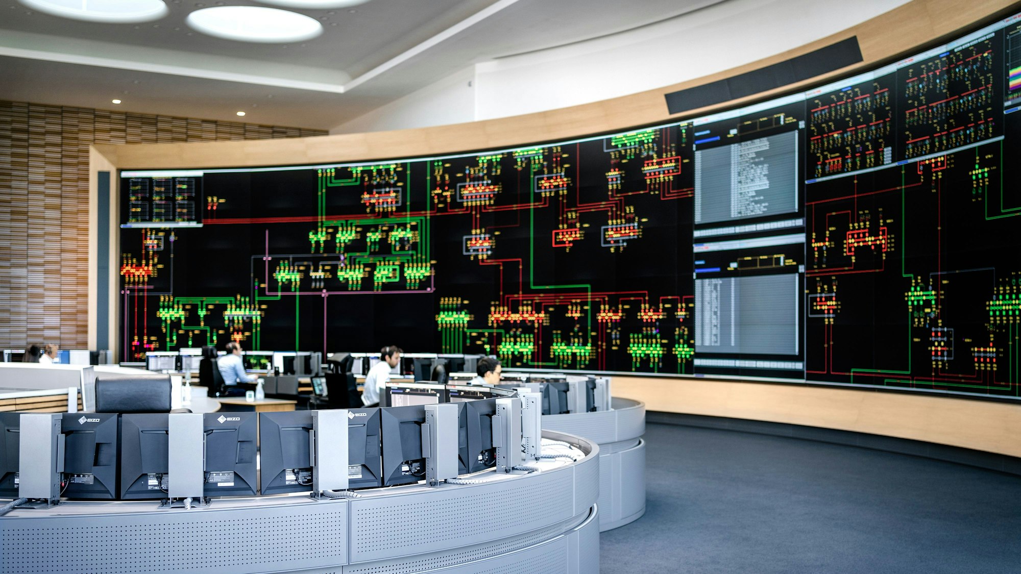 Das Foto zeigt die Hauptschaltleitung mit Arbeitsinseln vor dem großen Bildschirm.