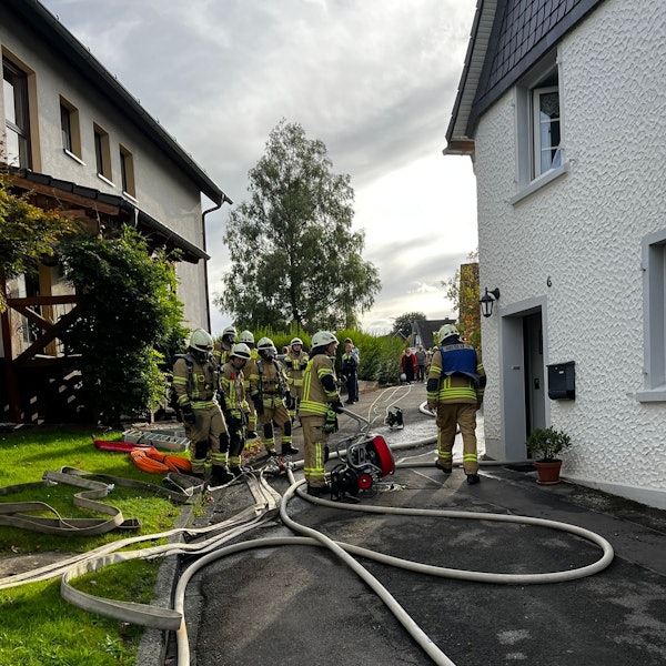 Mehrere Feuerwehrleute stehen vor einem Wohnhaus.