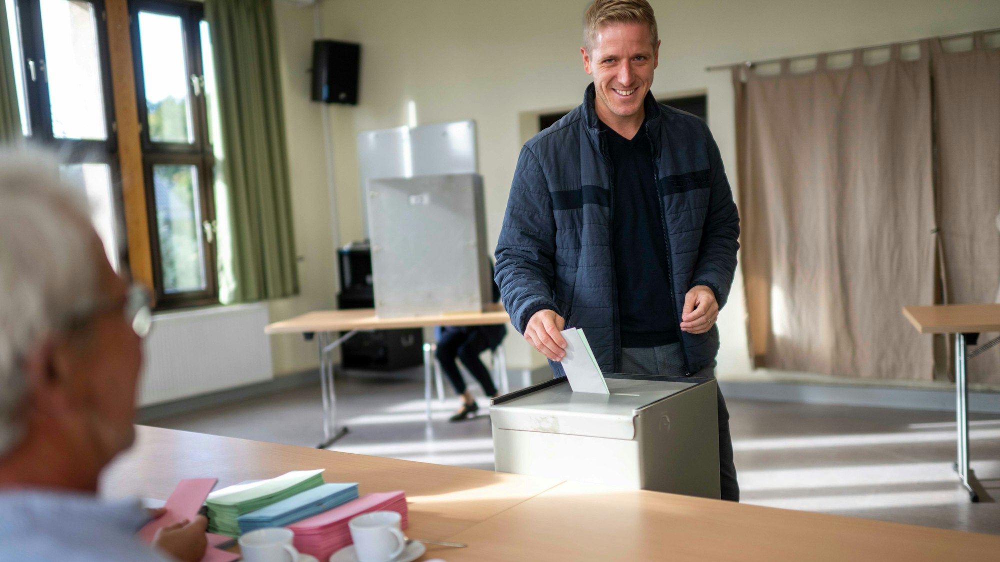 Landrat Markus Ramers (SPD) trägt eine blaue Jacke und gibt im Wahllokal in Blankenheim-Freilingen seine Stimmzettel in eine graue Wahlurne.