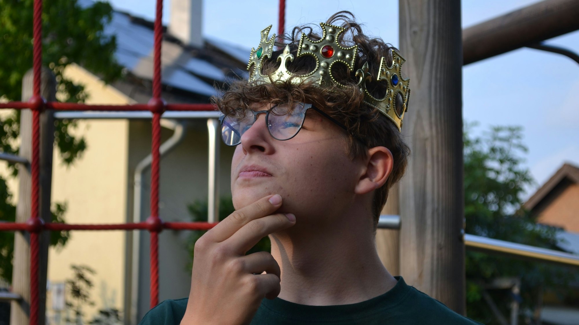 Ein Junge mit einer Königskrone auf dem Kopf. Er hat die Hand am Kinn, denkt offenbar nach.