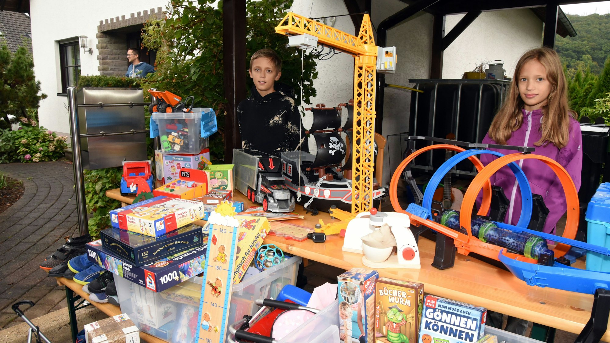 Zwei Kinder verkaufen vor der Haustüre Spielsachen bei einem Garagen-Trödelmarkt.