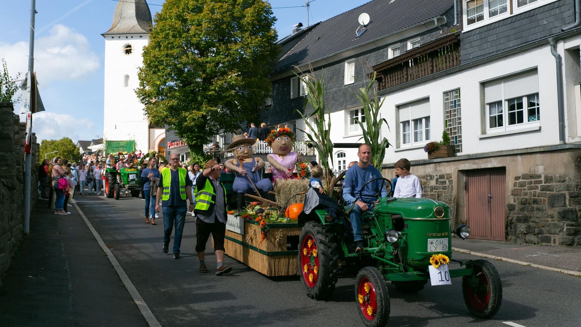 Eine Gruppe bei einem Erntezug. Ein historischer Traktor zieht einen geschmückten Wagen.