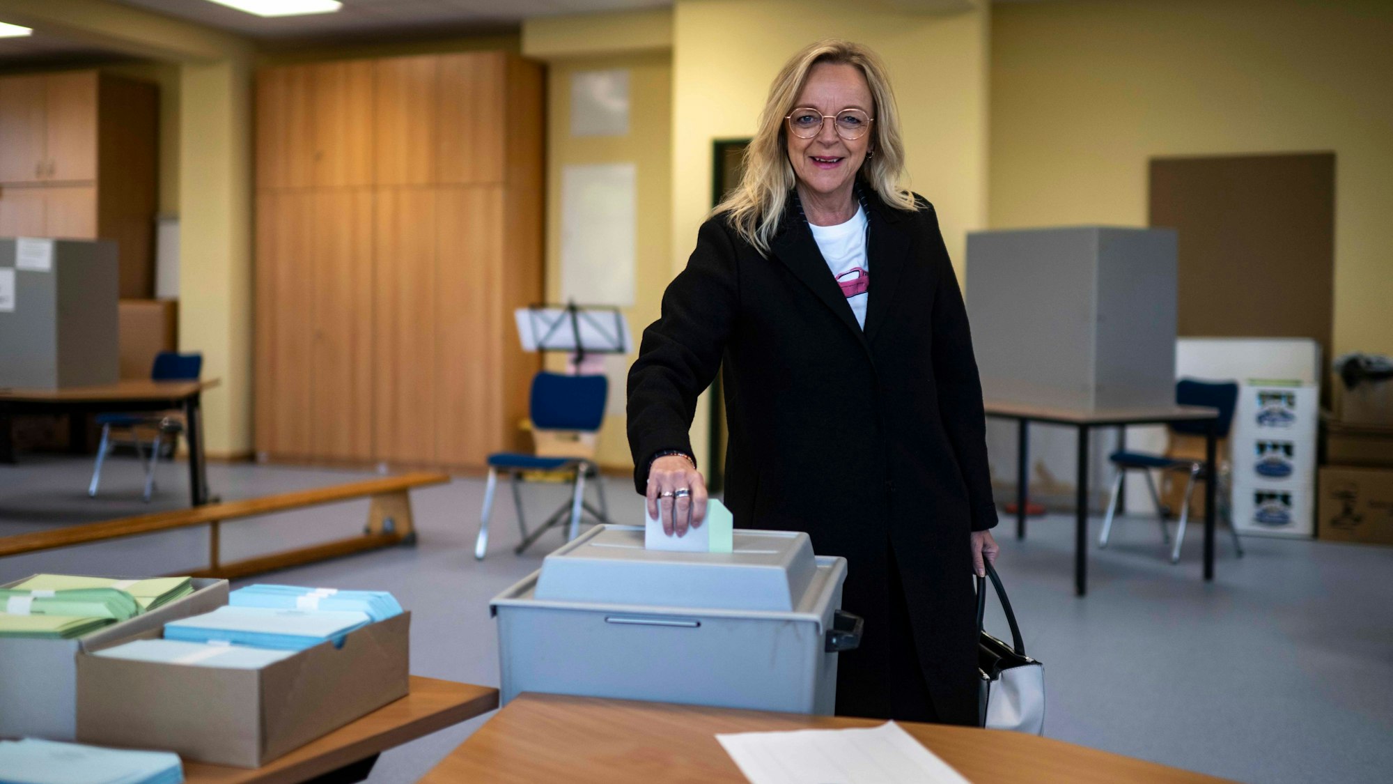 Sabine Preiser-Marian, die Landratskandidatin der CDU im Kreis Euskirchen, trägt einen schwarzen Mantel und gibt im Wahllokal in Bad Münstereifel-Arloff ihre Stimmzettel in eine graue Wahlurne.