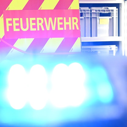 Ein Fahrzeug der Feuerwehr steht bei einem Einsatz auf einer Straße, während im Vordergrund das Blaulicht eines Polizeifahrzeugs zu sehen ist.