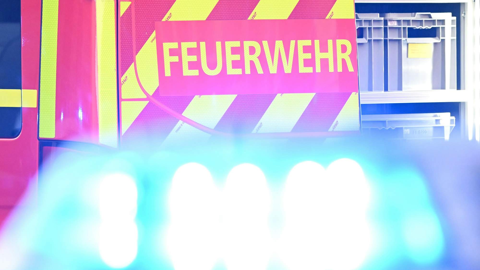 Ein Fahrzeug der Feuerwehr steht bei einem Einsatz auf einer Straße, während im Vordergrund das Blaulicht eines Polizeifahrzeugs zu sehen ist.