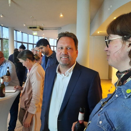 Ein Mann und eine Frau, im Hintergrund mehrere Personen an einem Stehtisch.