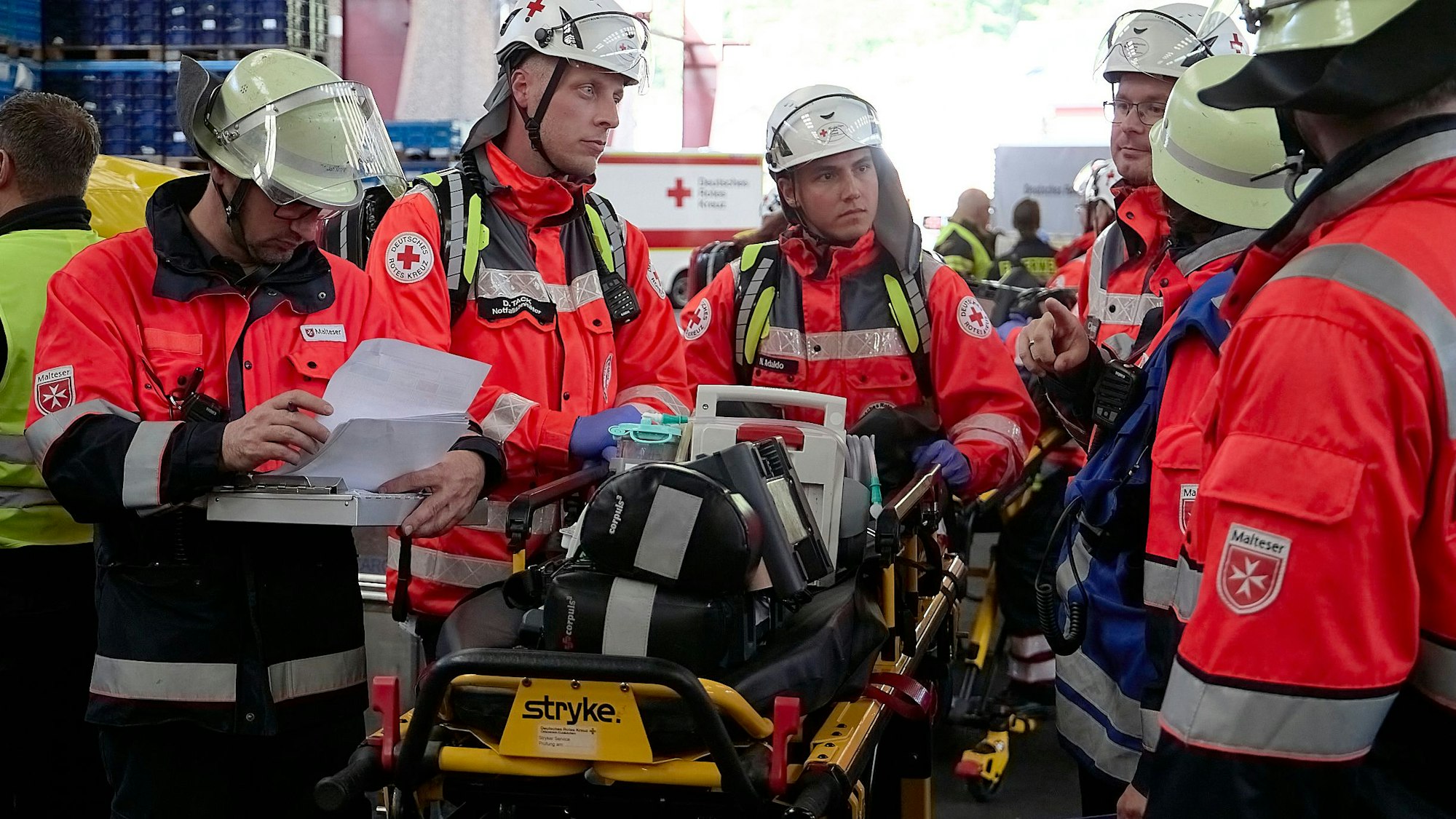 Sanitäter in roter Einsatzkleidung mit Helmen besprechen den Abtransport eines Verletzten.