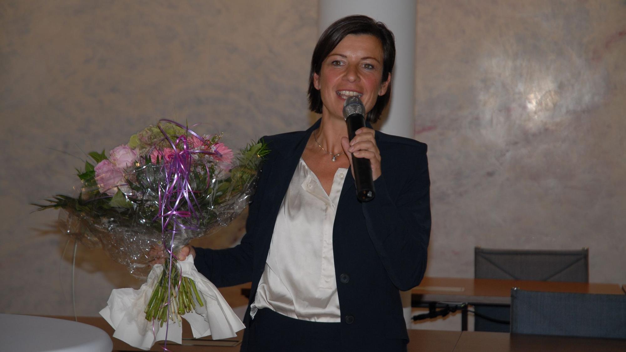 Eine Frau hält einen Blumenstrauß und spricht in ein Mikro.