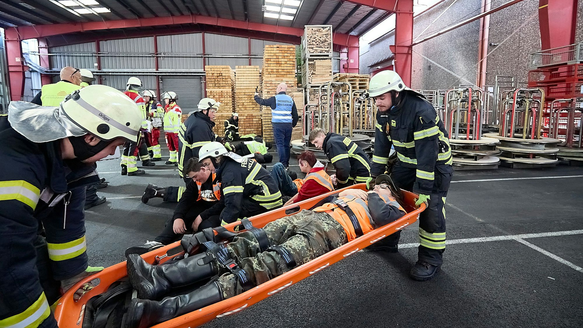 Zwei Feuerwehrleute transportieren einen Verletztendarstellern in einer Schleifkorbtrage durch die Werkhalle.