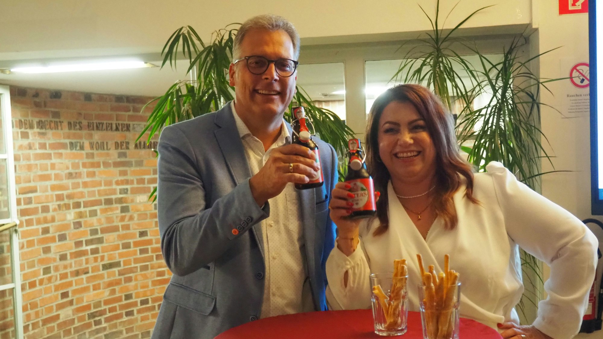 Ulf Hürtgen (l.) und lsabella Meurer prosten einander mit Bierflaschen zu.