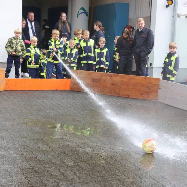 Eine Wasserfußball-Aktion bei einem Fest der Kinderfeuerwehr. Ein Junge spritzt mit Löschwasser aus einem Schlauch auf einen Fußball.