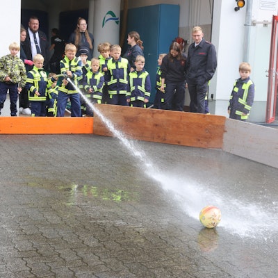 Eine Wasserfußball-Aktion bei einem Fest der Kinderfeuerwehr. Ein Junge spritzt mit Löschwasser aus einem Schlauch auf einen Fußball.