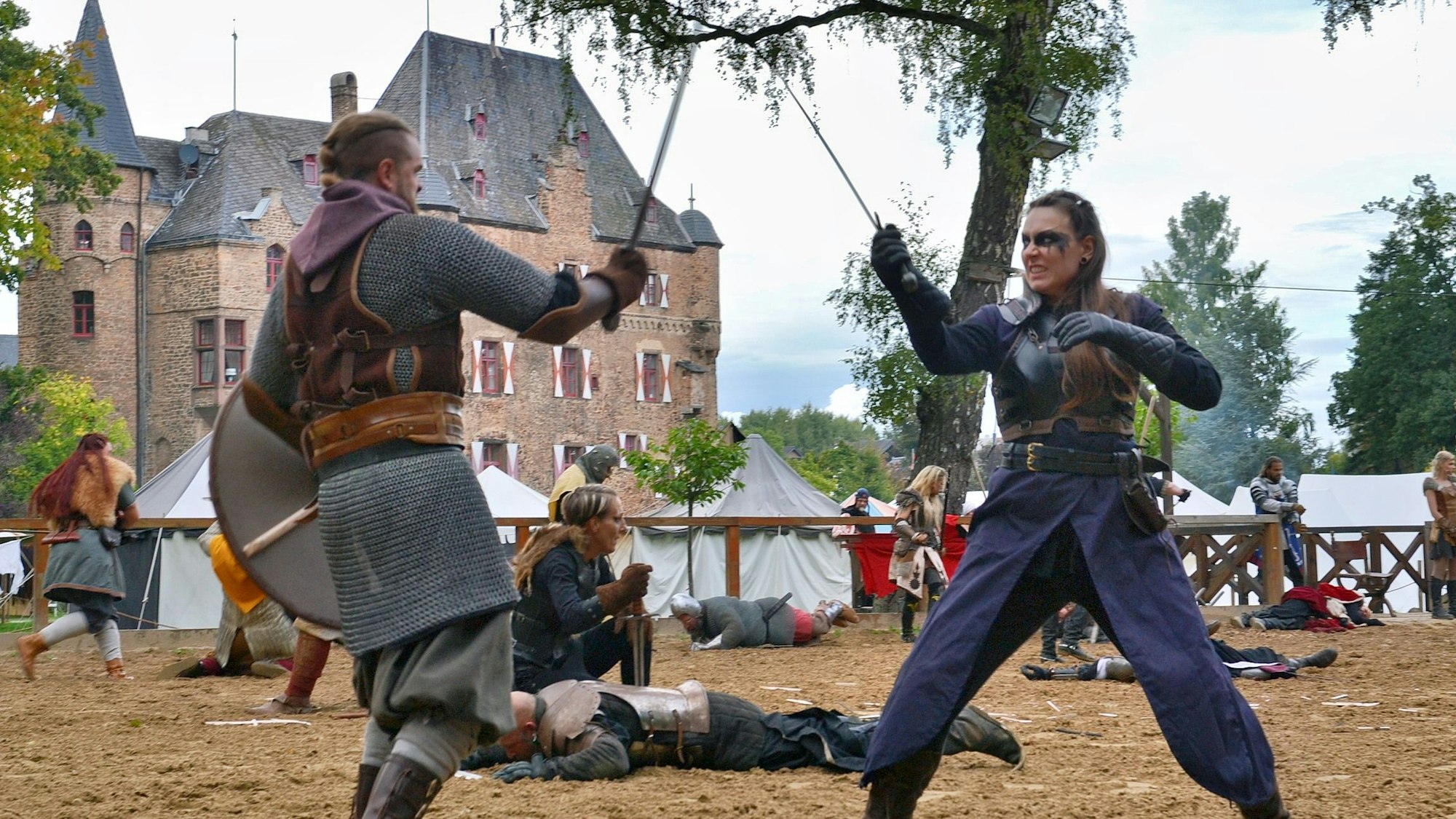 Vor der Kulisse der Burg Satzvey liefern sich ein Mann und eine Frau einen Schwertkampf.
