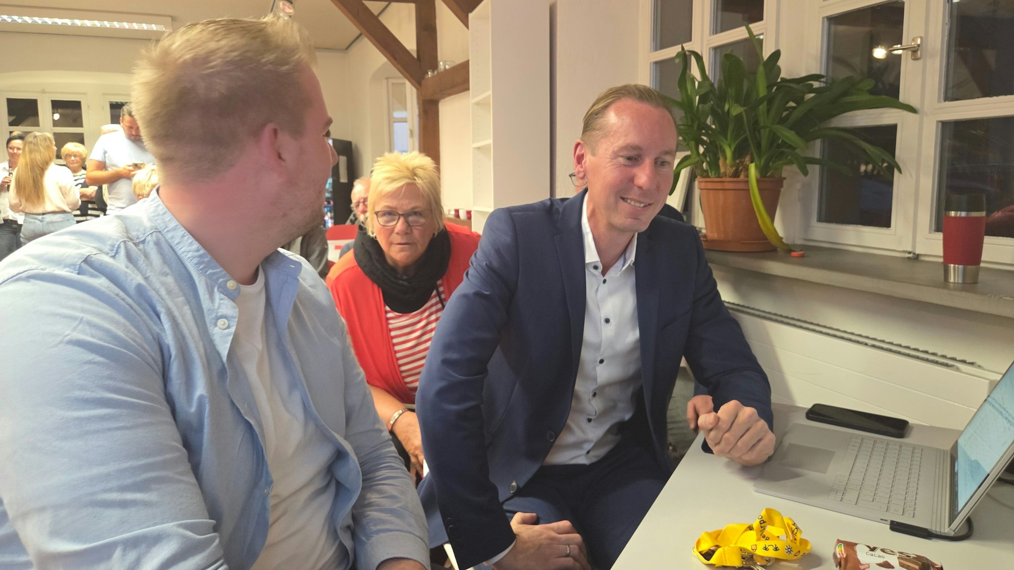 Zwei Männer und eine Frau an einem Schreibtisch mit einem aufgeklappten Laptop.