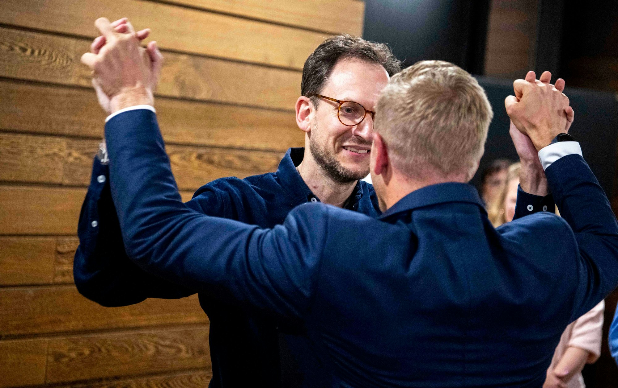 Das Bild zeigt die beiden Obengenannten, wie sie sich an den Händen fassen.