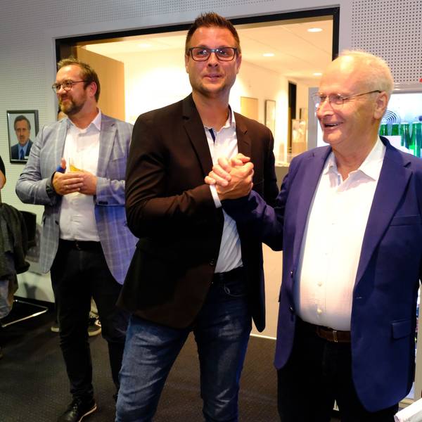 Hans-Peter Schick (r.) gratuliert Michael Fingel per Handschlag. Daneben stehen einige Personen und applaudieren.