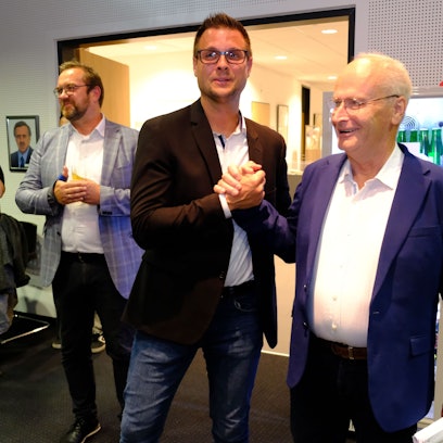 Hans-Peter Schick (r.) gratuliert Michael Fingel per Handschlag. Daneben stehen einige Personen und applaudieren.