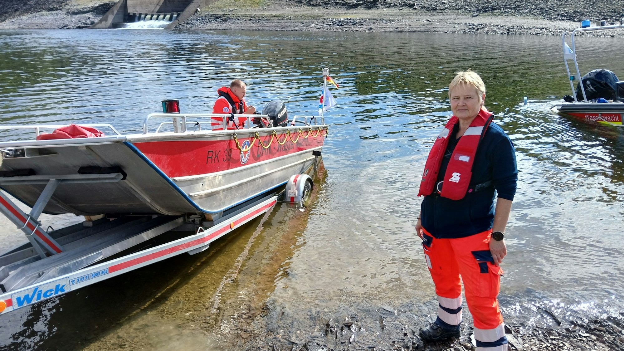 Kerstin von den Driesch trägt neben der DRK-Kleidung eine Rettungsweste. Sie steht am Ufer des Rursees an einem Rettungsboot, das von einem Anhänger zu Wasser gelassen wird.