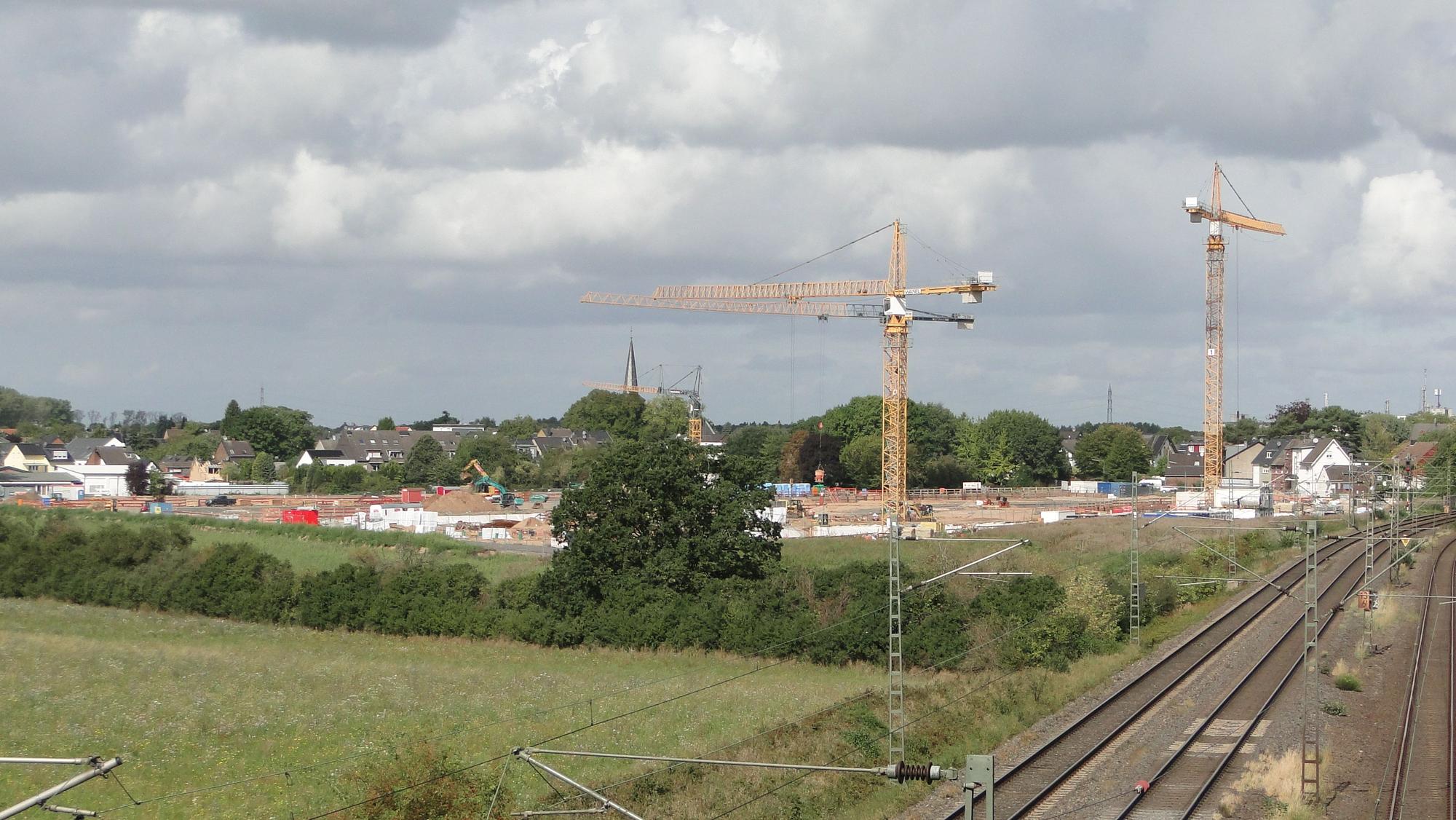 Auf einer großflächigen Baustelle stehen Kräne und Baufahrzeuge.