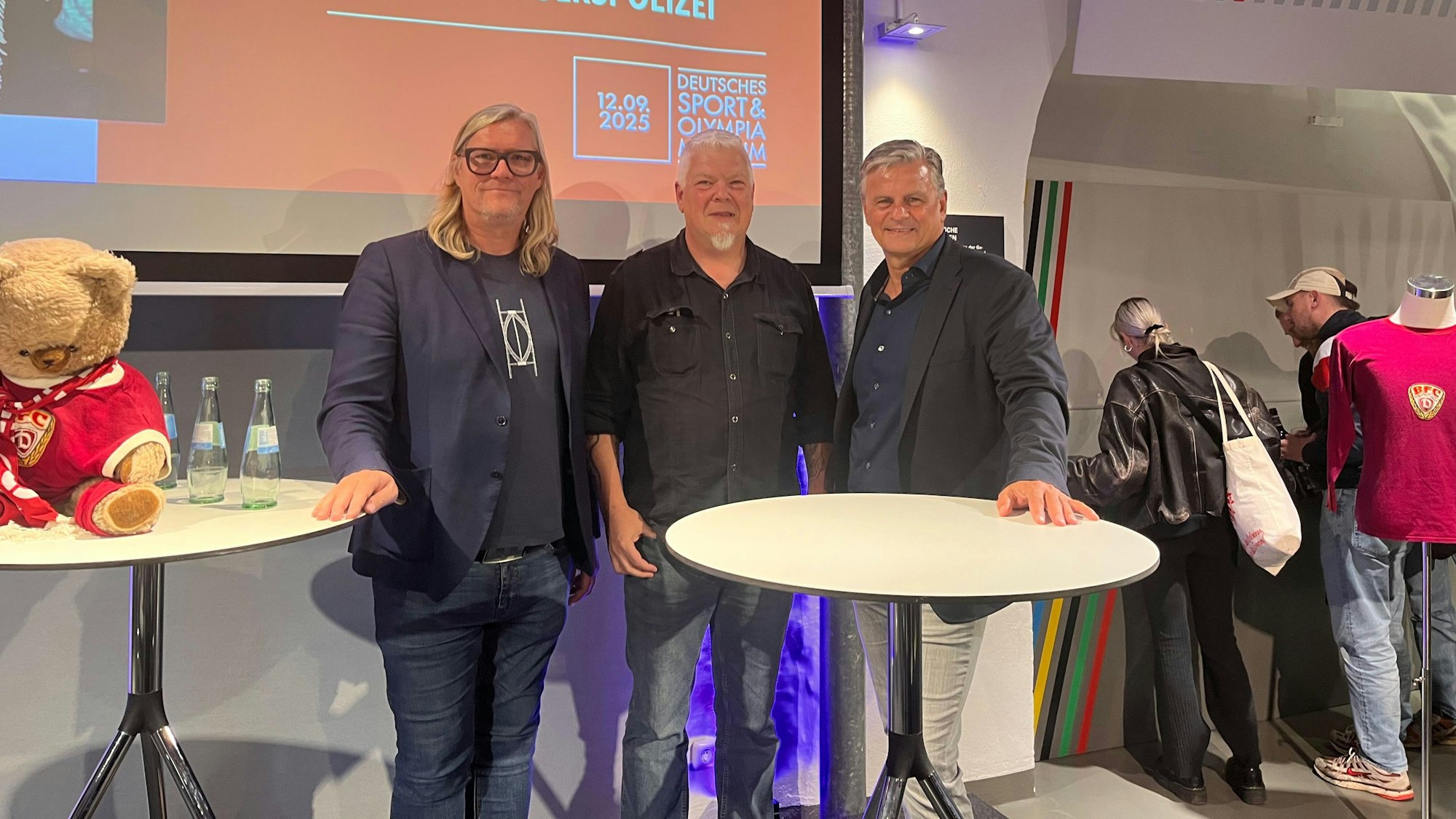 Drei Männer stehen an einem Stehtisch.