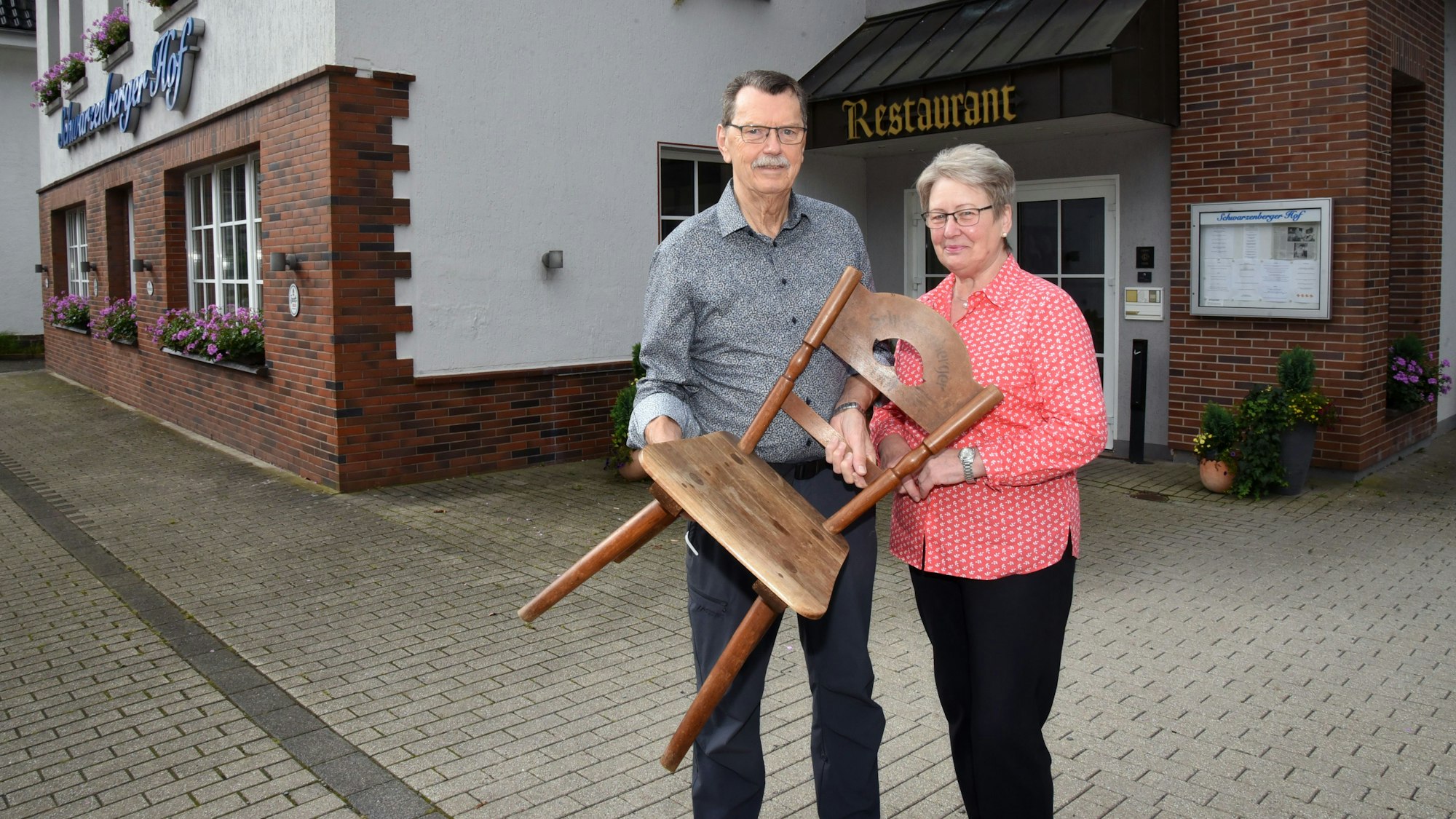 Die Inhaber der Restaurants, Angelika und Klaus Jaeger, feiern 100 Jahre Schwarzenberger Hof, hier mit einem Holzstuhl aus alter Zeit.