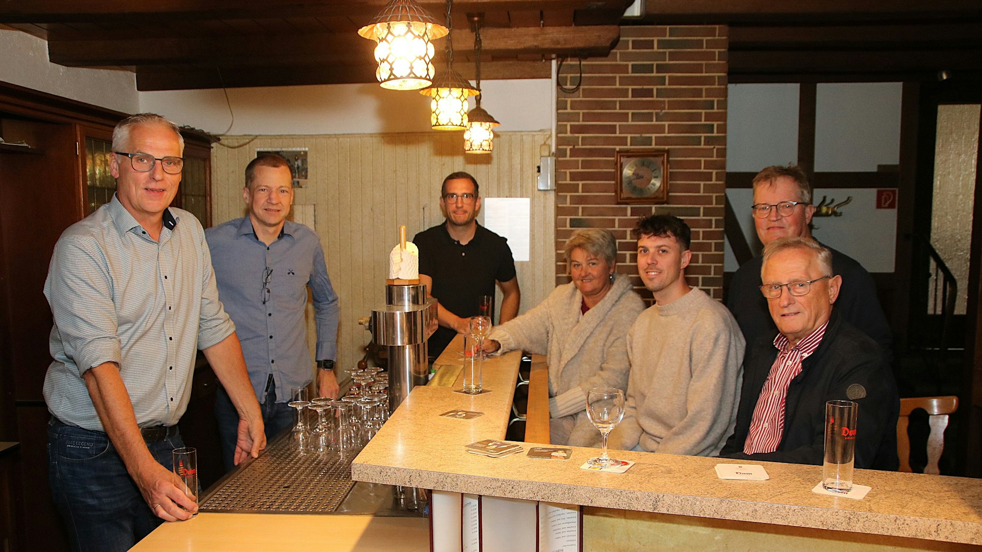 Eine Gruppe steht in einer Kneipe an und hinter dem Tresen.