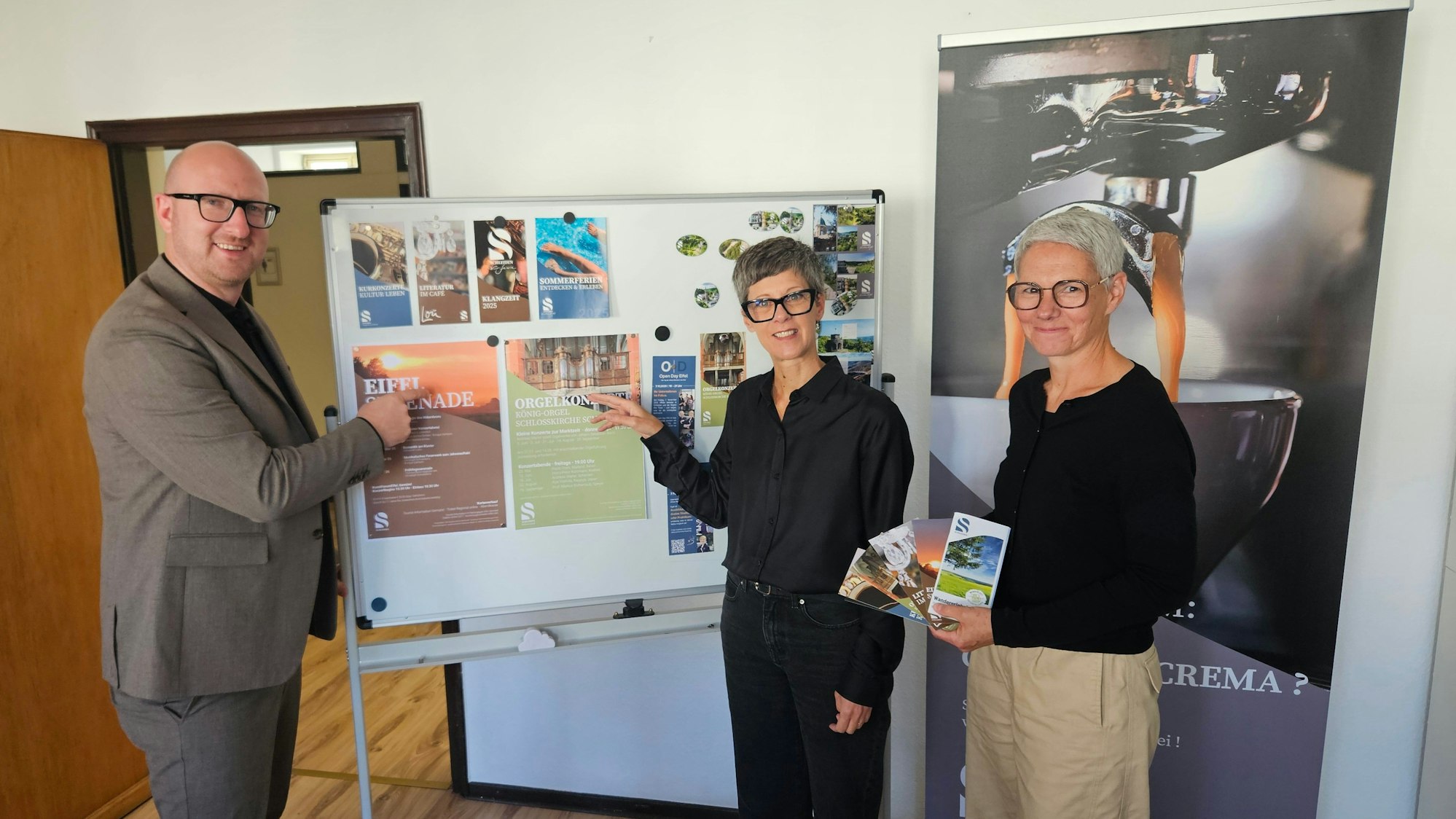 Bürgermeister Ingo Pfennings, Bianka Renn und Stefanie Hermes stehen vor einer Stellwand mit Werbeplakaten von den Veranstaltungen.
