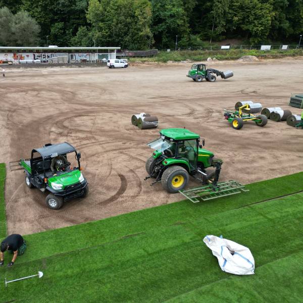 Eine Firma verlegt Rollrasen auf einem Sportplatz.