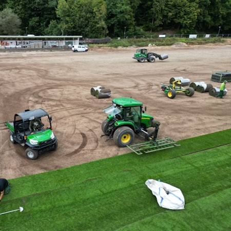 Eine Firma verlegt Rollrasen auf einem Sportplatz.
