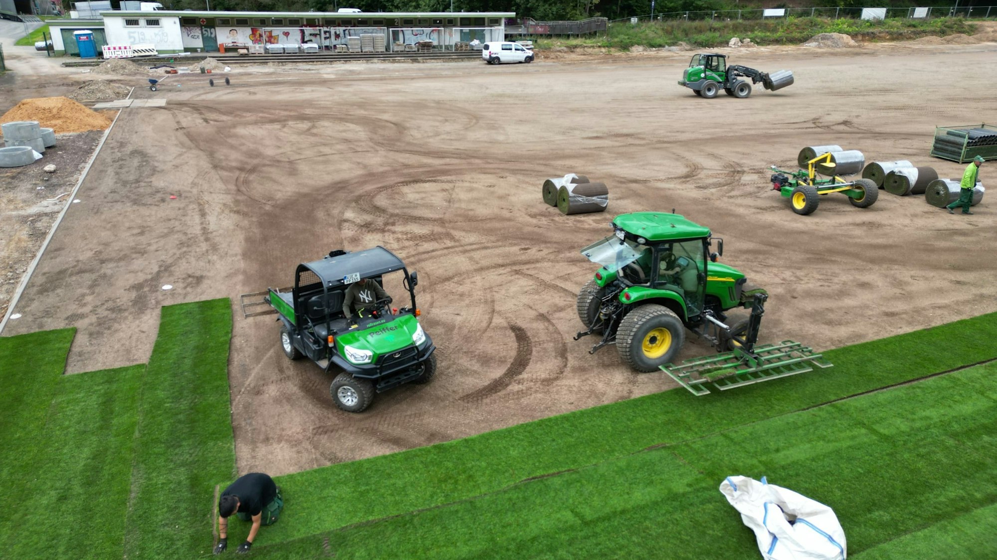 Ein Team legt Rollrasen auf dem Spielfeld eines Sportplatzes.