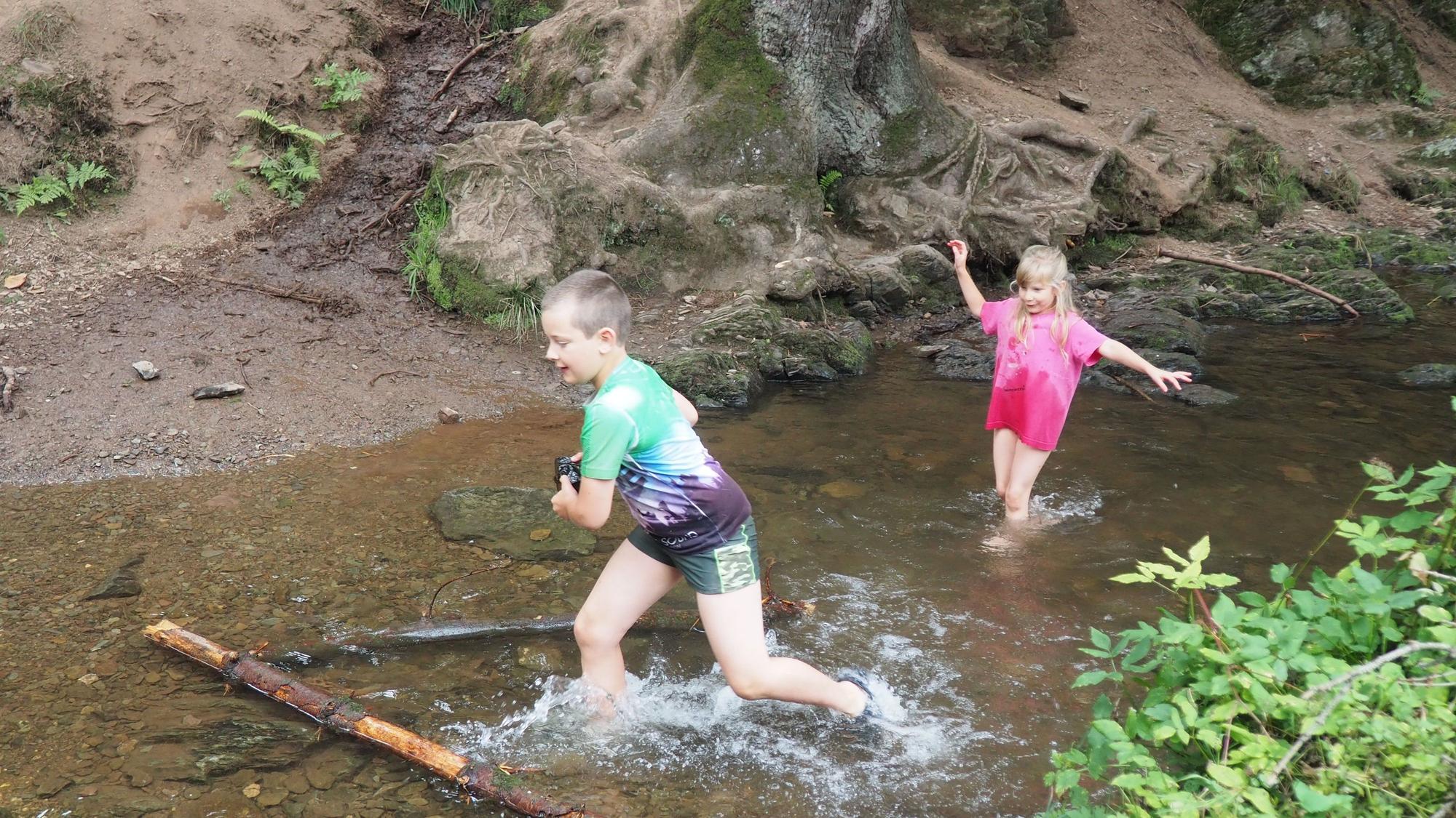 Zwei Kinder spielen im seichten Wasser eines Baches.