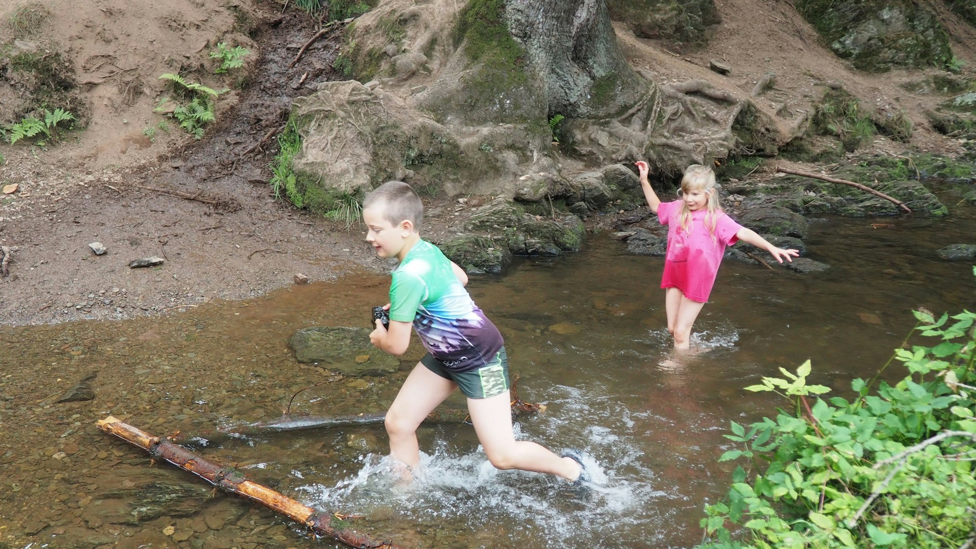 Zwei Kinder spielen im seichten Wasser eines Baches.