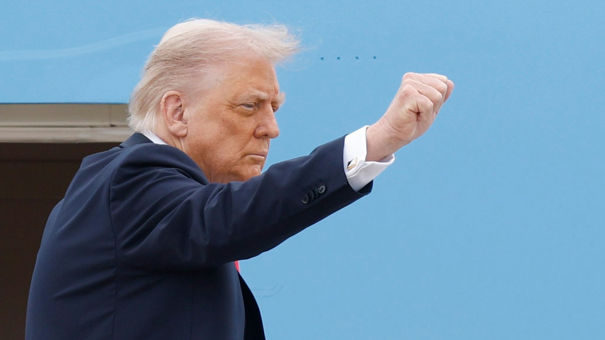 Trump steht vor blauem Hintergrund und streckt seine Faust nach vorn.