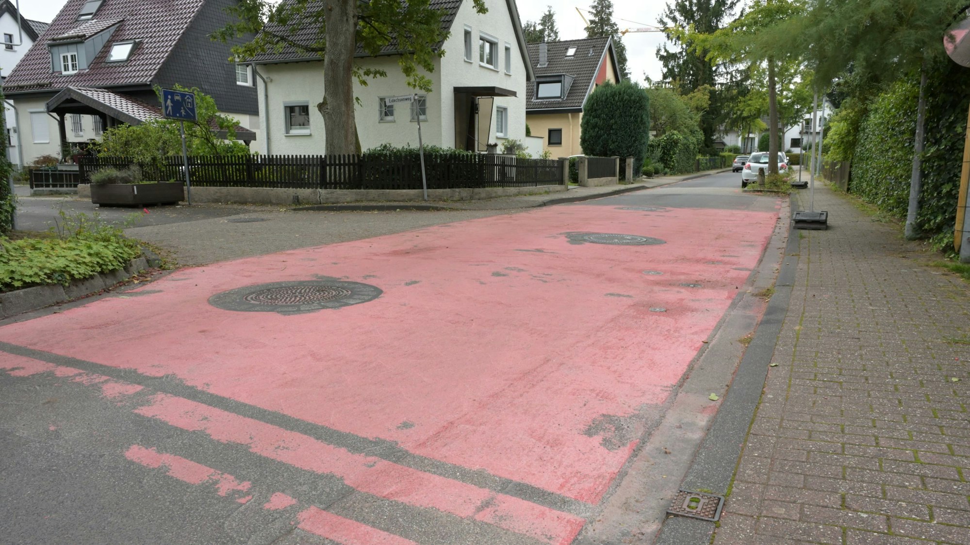 Eine Anwohnerstraße mit rotem Asphalt an einer Einmündung.