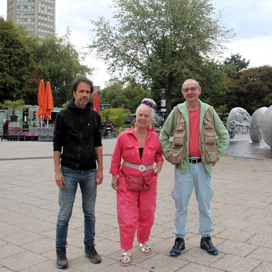 Zwei Männer und eine Frau stehen auf vor dem Brunnen auf dem Ebertplatz.