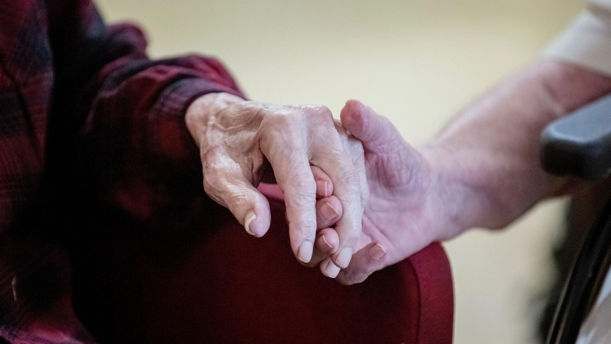 Das Foto zeigt die Hand einer alten Person, die in der Hand einer Jüngeren liegt.