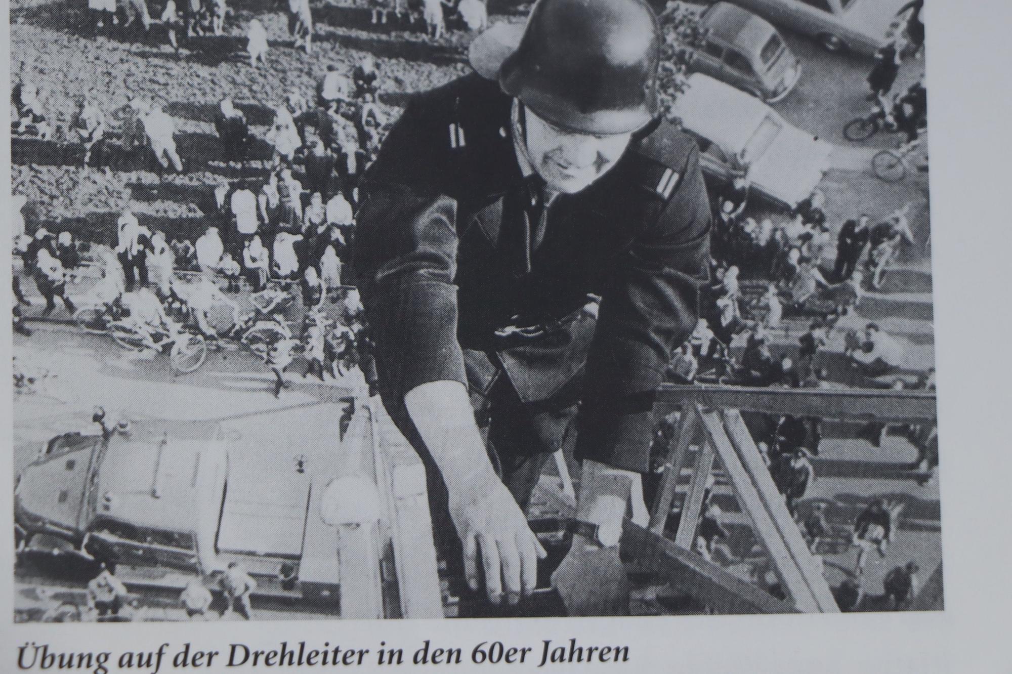 Auf dem Bild ist ein Mann auf einer hohen Drehleiter zu sehen. Viele Menschen schauen von unten zu.