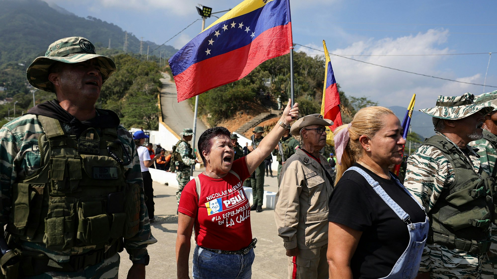 Eine Frau, Mitte, hält eine Nationalflagge während einer Militärübung hoch.