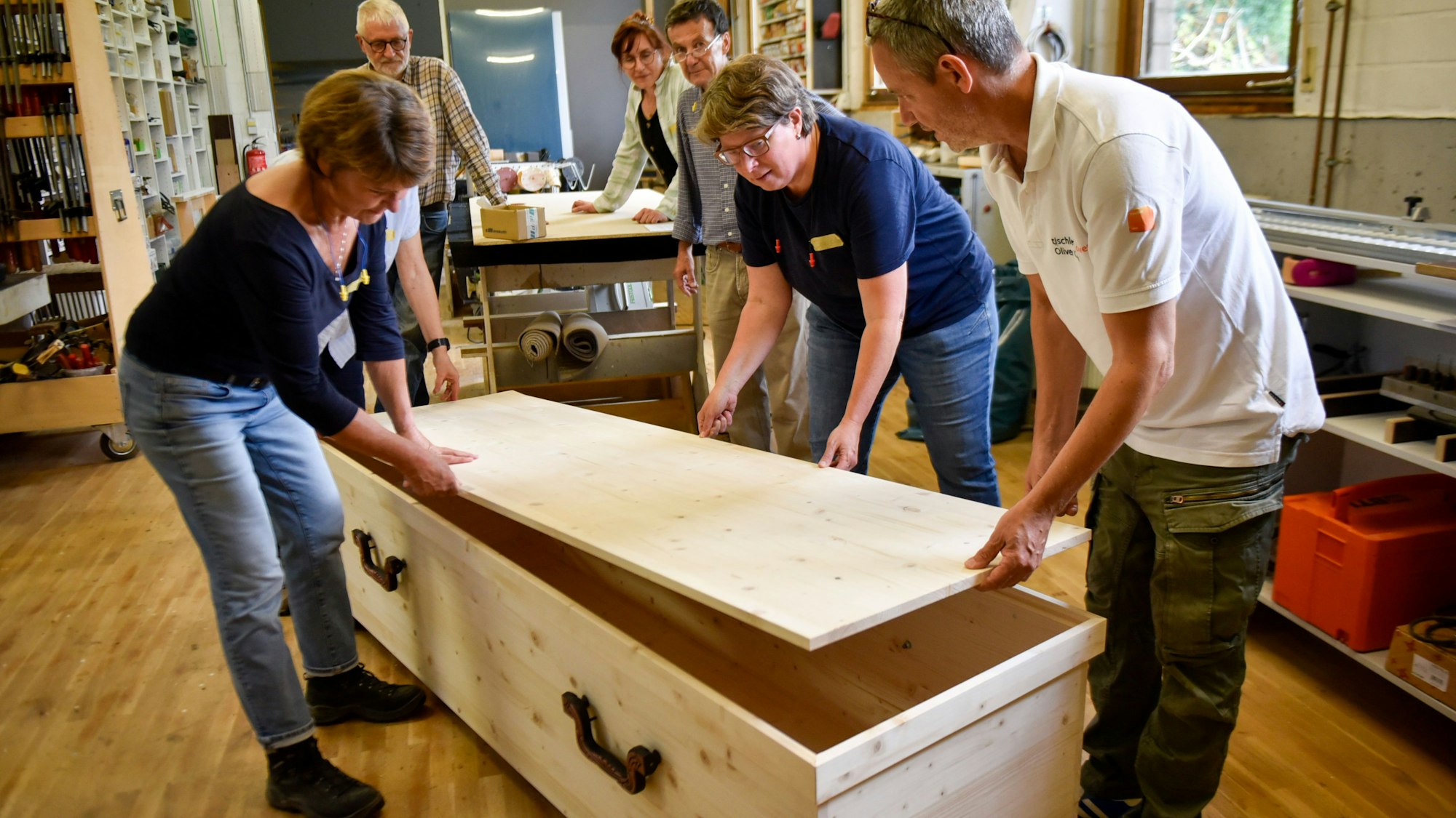 Auf dem Bild sind Teilnehmer eines Workshops mit einem selbst gebauten Holzsarg zu sehen.