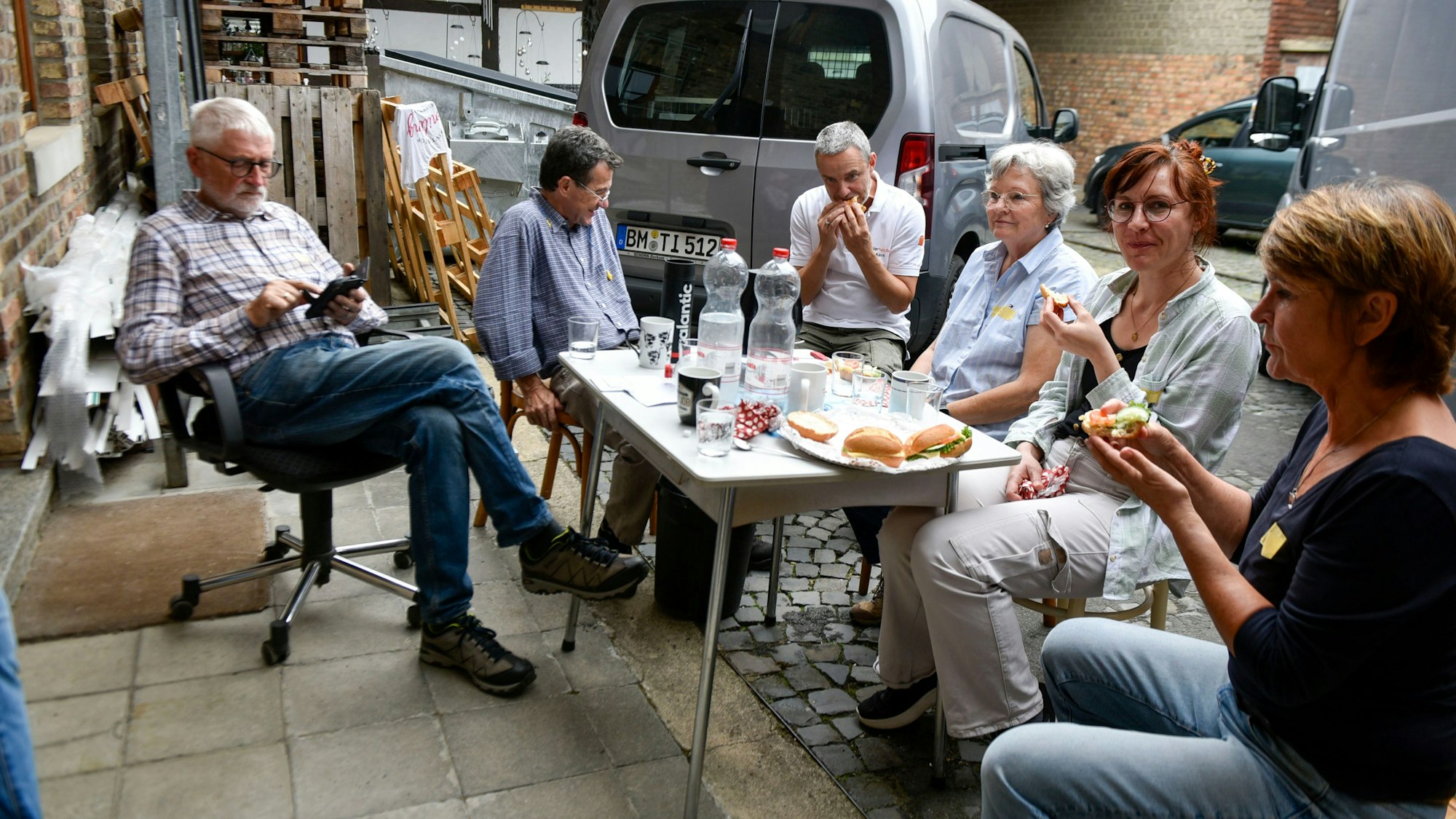 Auf dem Bild sind Menschen zu sehen, die in einem Werkstatthof sitzen und Brötchen essen.