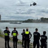 Polizei am Rhein, darüber ein Hubschrauber.