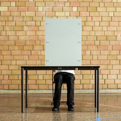 Ein Mann sitzt hinter einer Wahlkabine.