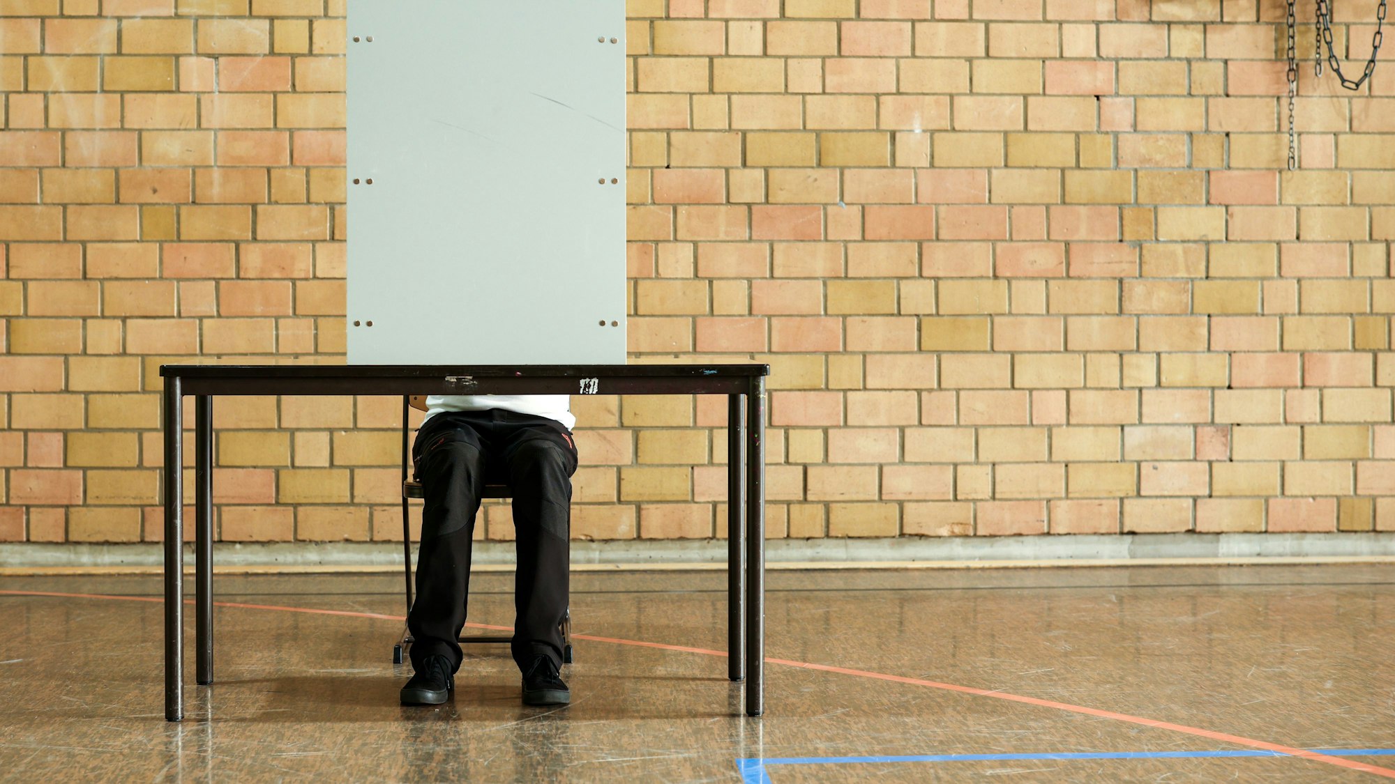 Ein Mann sitzt hinter einer Wahlkabine.