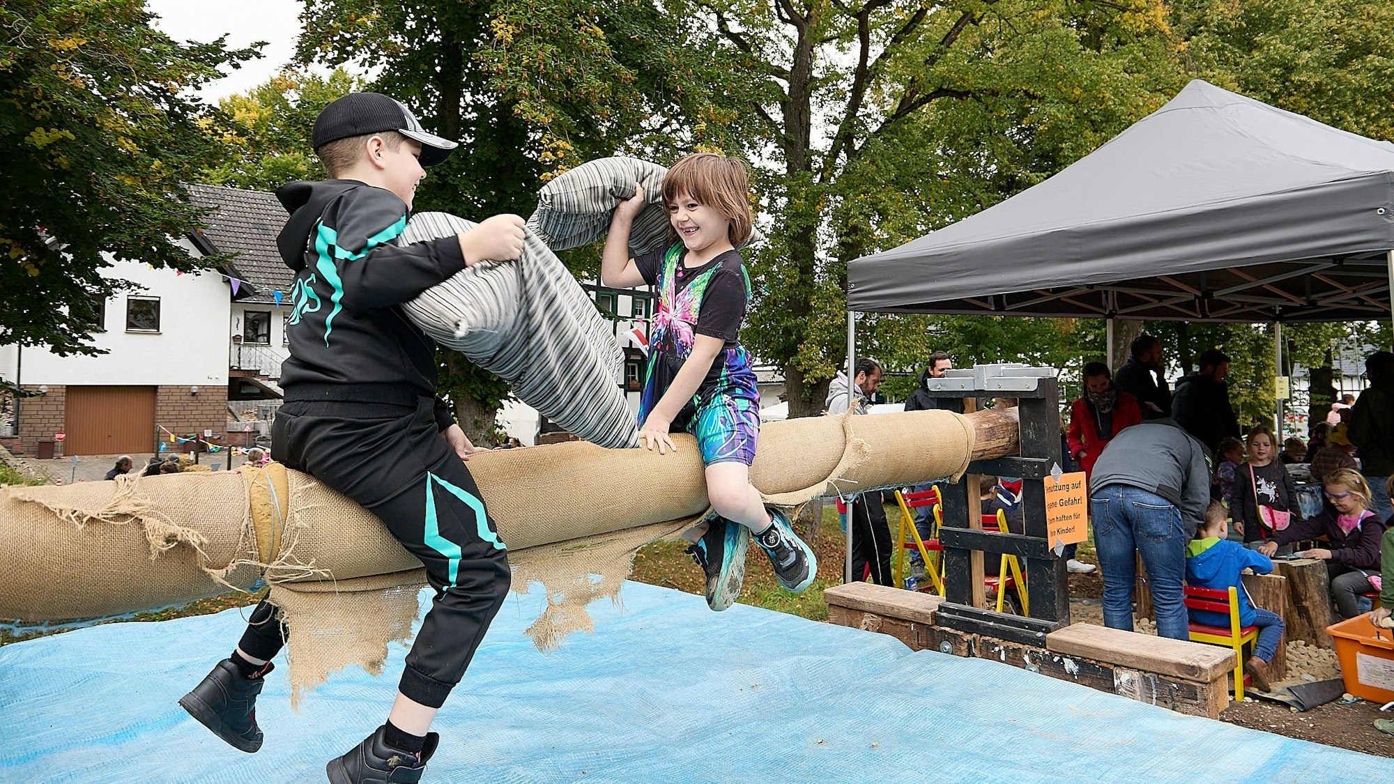 Zwei Kinder sitzen auf einem Balken und bekämpfen einander mit Kissen.