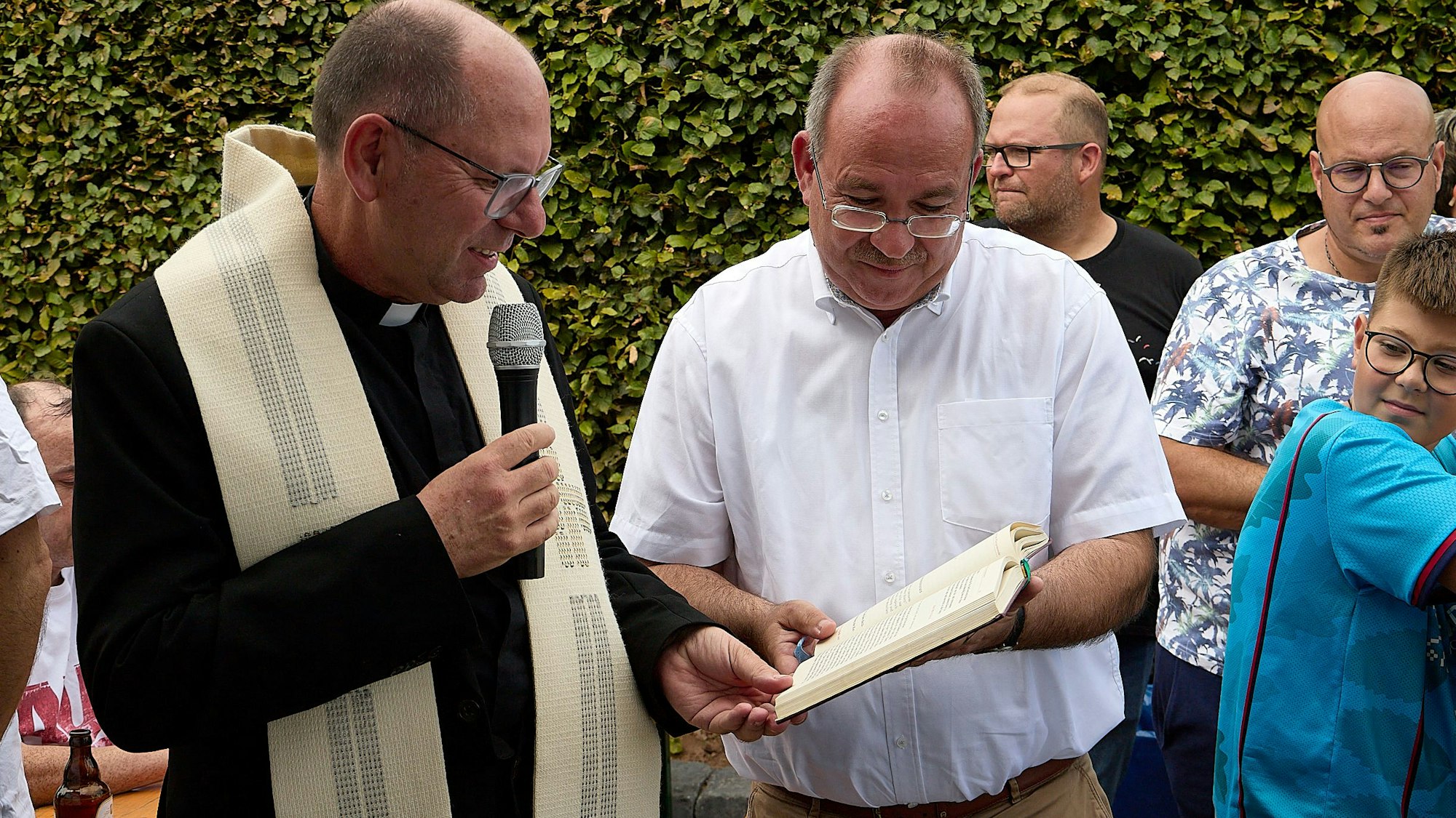 Der Pfarrer liest aus einem Buch, das der Landtagsabgeordnete vor ihn hält.